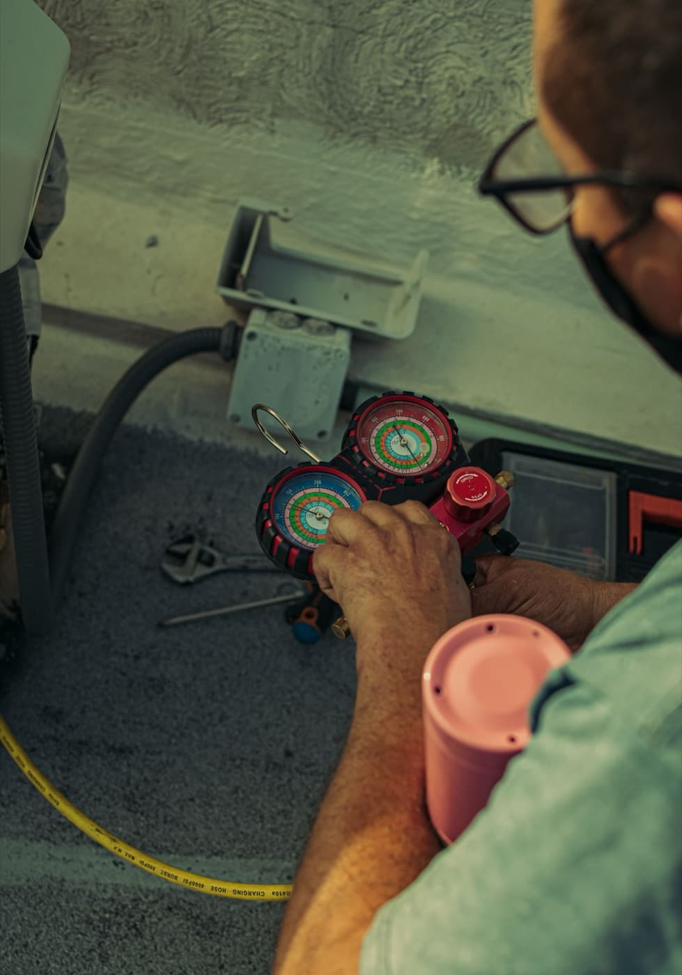 Technician's gloved hands reading refrigerant gauges during an AC repair