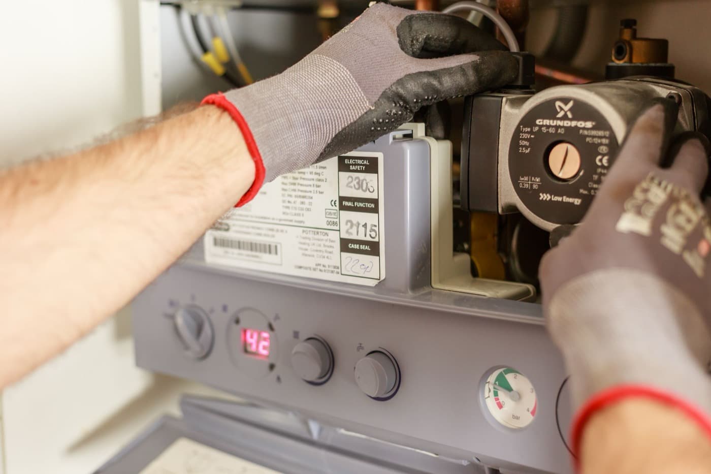 Technician's gloved hands working inside an open heating system cabinet