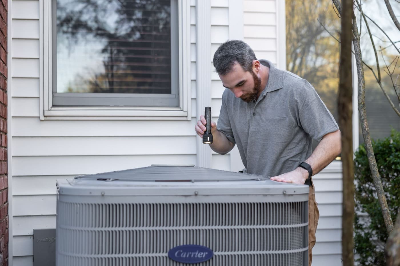 Technician inspecting a residential outdoor condenser unit with a flashlight