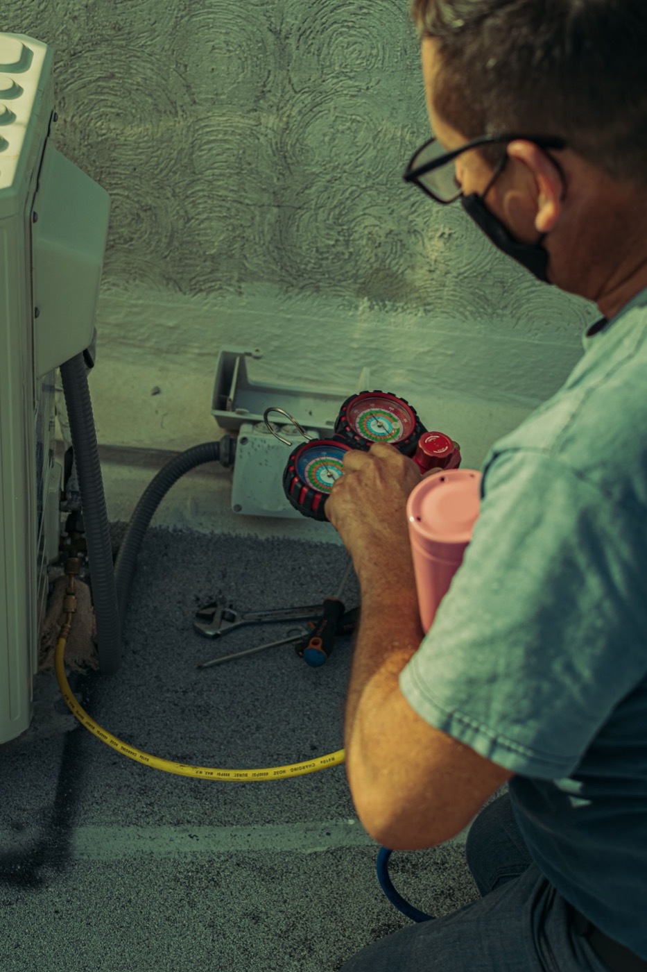 HVAC technician kneeling outdoors with a toolbox, connecting service gauges