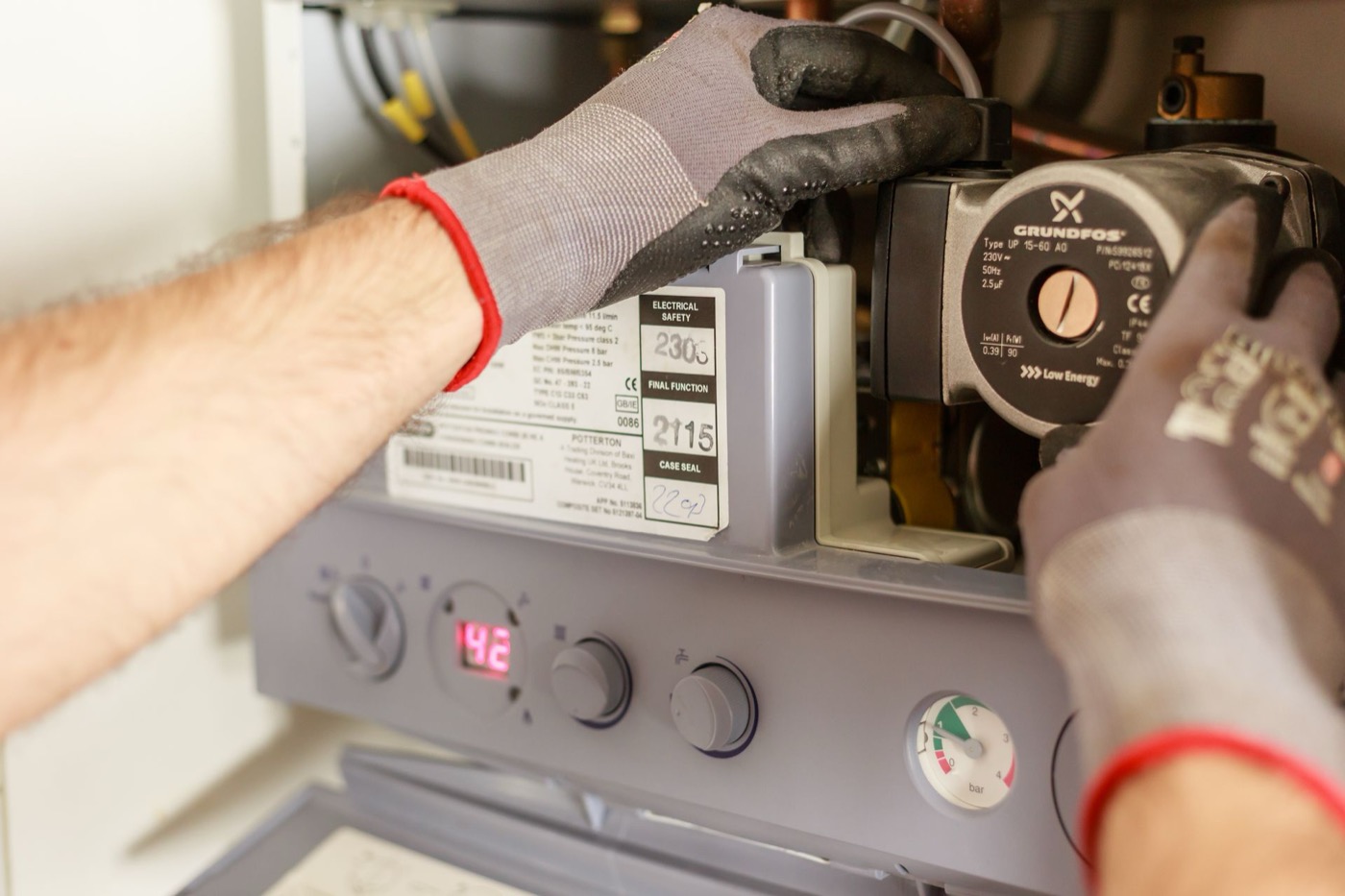 Technician's gloved hands working inside an open heating system cabinet