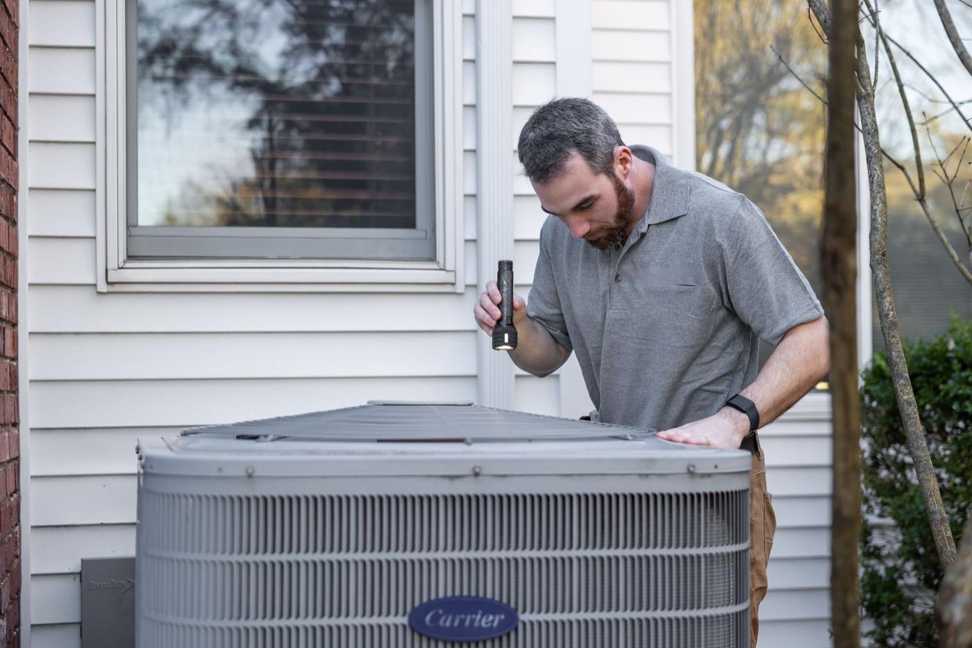 Technician inspecting a residential outdoor condenser unit with a flashlight